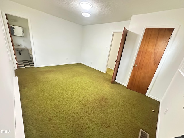 unfurnished bedroom with dark colored carpet, sink, connected bathroom, and a textured ceiling