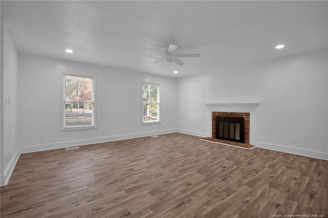 unfurnished living room featuring hardwood / wood-style floors, a textured ceiling, a brick fireplace, and ceiling fan