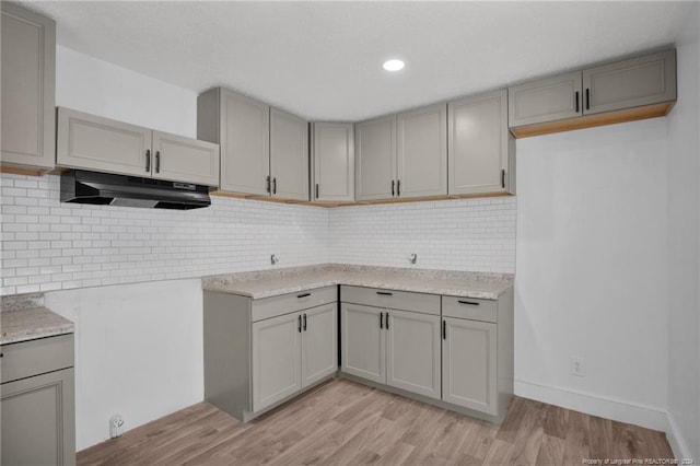 kitchen with tasteful backsplash, gray cabinets, light stone counters, and light wood-type flooring