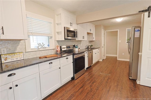 kitchen with dark wood-type flooring, white cabinetry, stainless steel appliances, dark stone counters, and sink