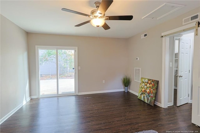 empty room featuring ceiling fan, a barn door, and dark wood-type flooring