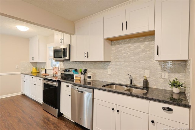 kitchen with appliances with stainless steel finishes, tasteful backsplash, dark stone countertops, white cabinets, and sink