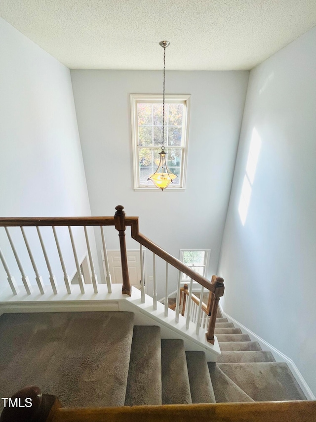 staircase featuring a textured ceiling and carpet flooring