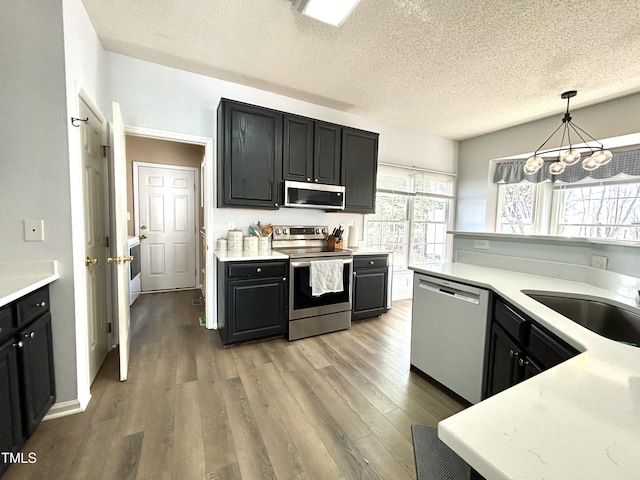 kitchen with sink, appliances with stainless steel finishes, a textured ceiling, decorative light fixtures, and light wood-type flooring