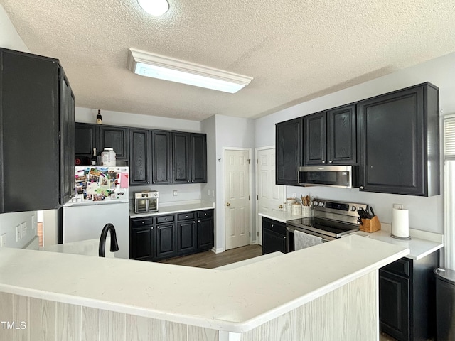 kitchen with appliances with stainless steel finishes, kitchen peninsula, hardwood / wood-style floors, and a textured ceiling