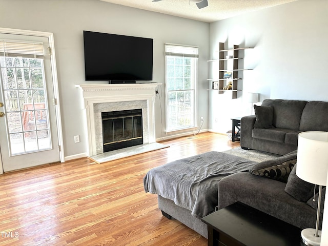 living room featuring ceiling fan, a fireplace, light hardwood / wood-style flooring, and a textured ceiling