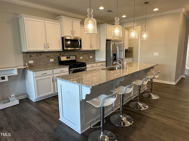 kitchen featuring stainless steel appliances, a kitchen island with sink, sink, white cabinetry, and hanging light fixtures