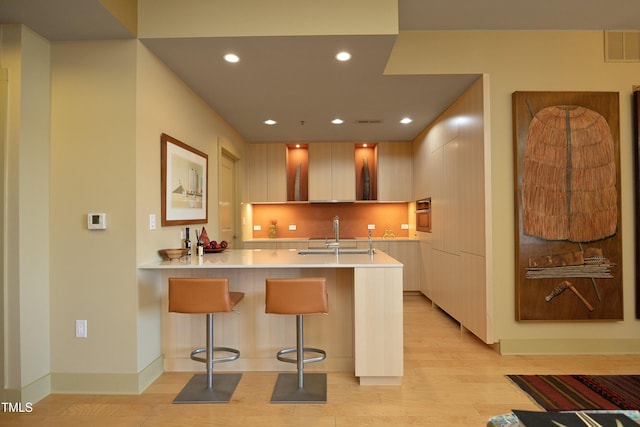 kitchen featuring light brown cabinets, sink, light hardwood / wood-style flooring, kitchen peninsula, and a kitchen bar