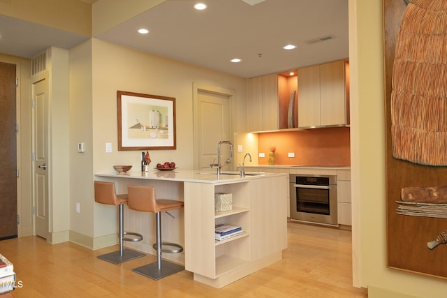 kitchen featuring a kitchen bar, kitchen peninsula, sink, light hardwood / wood-style flooring, and oven