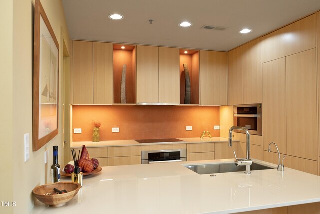 kitchen featuring light brown cabinetry, oven, and sink