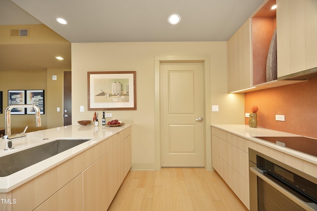 kitchen featuring stainless steel oven, sink, stovetop, light hardwood / wood-style floors, and light brown cabinetry