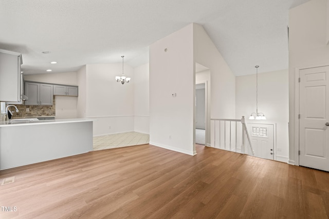 unfurnished living room featuring light hardwood / wood-style floors, an inviting chandelier, lofted ceiling, and sink