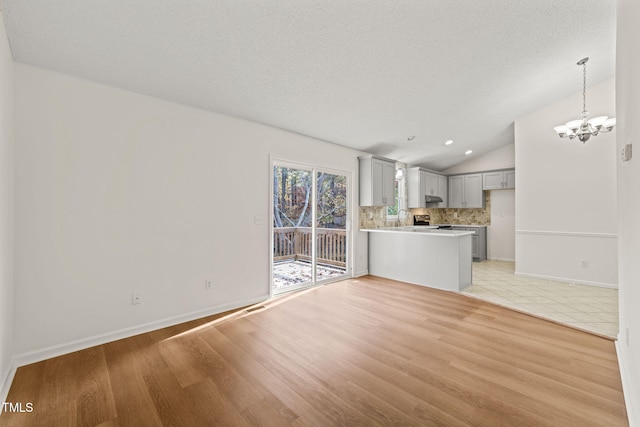 unfurnished living room with a textured ceiling, an inviting chandelier, light hardwood / wood-style flooring, and lofted ceiling