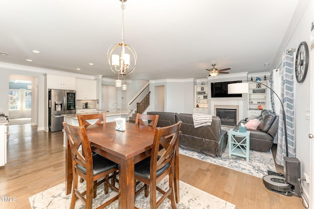 dining room featuring crown molding, sink, ceiling fan with notable chandelier, and light wood-type flooring