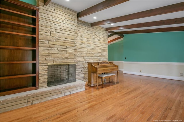 unfurnished living room featuring hardwood / wood-style floors, lofted ceiling with beams, a stone fireplace, and built in features