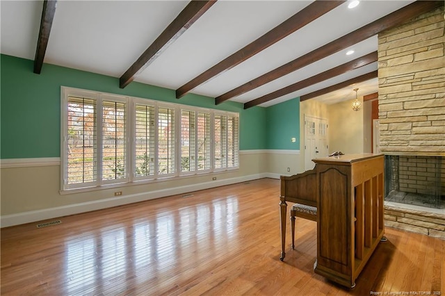 interior space with beamed ceiling, a chandelier, a fireplace, and light hardwood / wood-style flooring