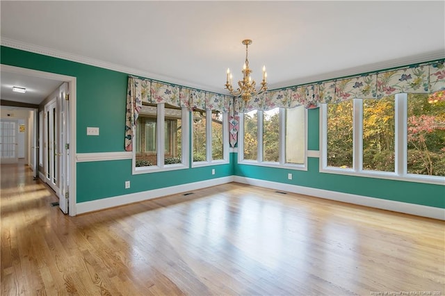 unfurnished dining area featuring a chandelier, light hardwood / wood-style floors, a wealth of natural light, and ornamental molding