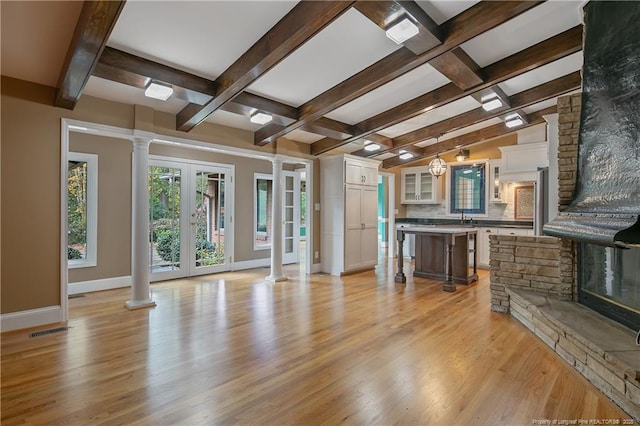 unfurnished living room featuring sink, a stone fireplace, light hardwood / wood-style flooring, and french doors