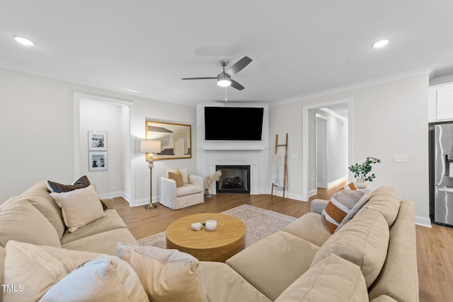 living room featuring a fireplace, light wood-type flooring, ceiling fan, and ornamental molding