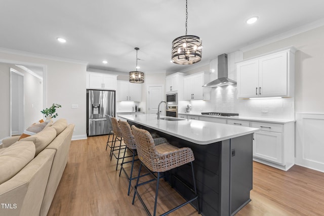 kitchen featuring light hardwood / wood-style flooring, wall chimney exhaust hood, an island with sink, white cabinetry, and stainless steel appliances