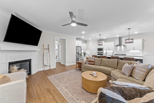 living room with ceiling fan with notable chandelier, light hardwood / wood-style flooring, ornamental molding, and sink