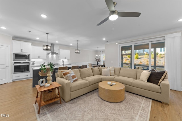 living room with ceiling fan with notable chandelier, light wood-type flooring, and crown molding