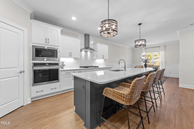 kitchen with white cabinetry, sink, hanging light fixtures, wall chimney range hood, and appliances with stainless steel finishes