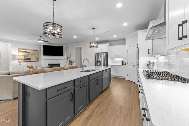 kitchen featuring appliances with stainless steel finishes, sink, a center island with sink, white cabinets, and hanging light fixtures