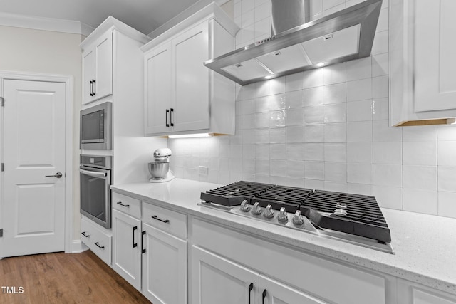 kitchen with appliances with stainless steel finishes, hardwood / wood-style flooring, white cabinetry, and wall chimney exhaust hood