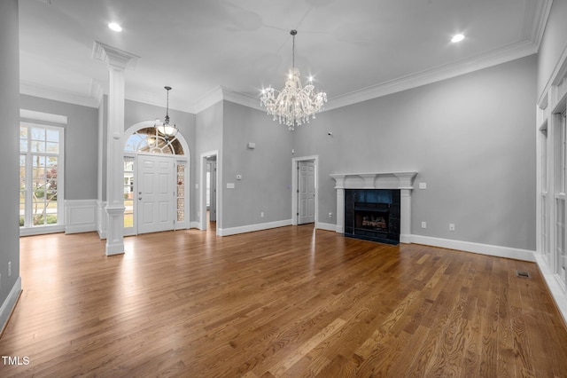 unfurnished living room featuring a tile fireplace, an inviting chandelier, decorative columns, crown molding, and hardwood / wood-style floors