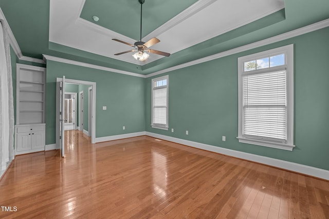 empty room featuring a raised ceiling, crown molding, and light hardwood / wood-style floors