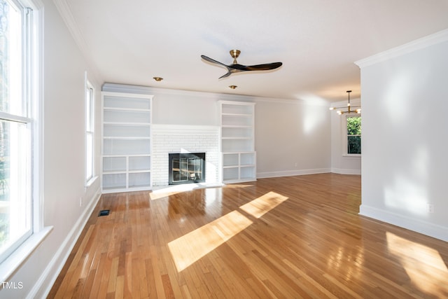 unfurnished living room featuring hardwood / wood-style floors, ceiling fan with notable chandelier, a brick fireplace, and ornamental molding