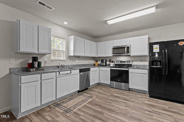 kitchen featuring stainless steel appliances, white cabinetry, light hardwood / wood-style floors, and sink