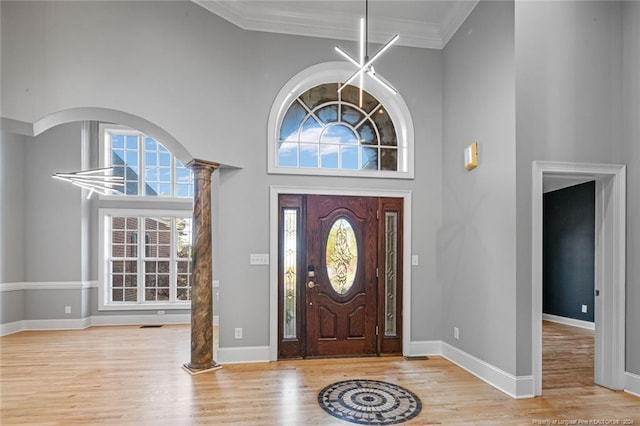 foyer with a wealth of natural light, crown molding, light hardwood / wood-style flooring, and a towering ceiling