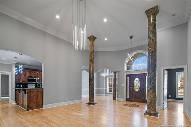 foyer entrance with ornate columns, crown molding, a towering ceiling, and light hardwood / wood-style floors