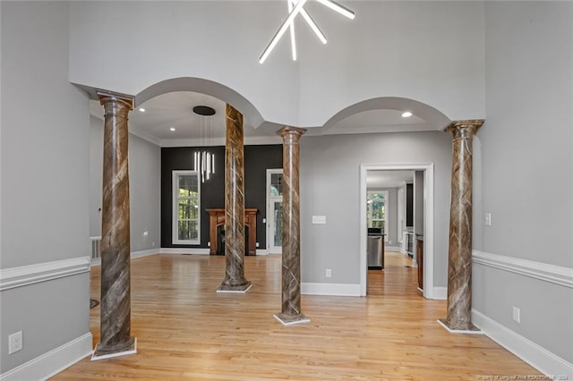 unfurnished living room with light hardwood / wood-style floors, ornate columns, and crown molding