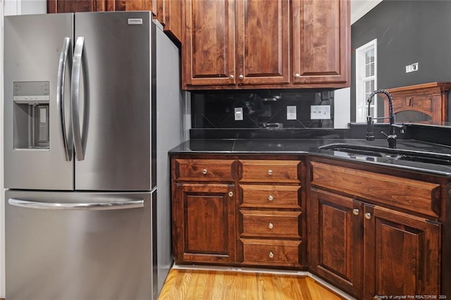 kitchen featuring sink, stainless steel refrigerator with ice dispenser, dark stone counters, decorative backsplash, and light wood-type flooring