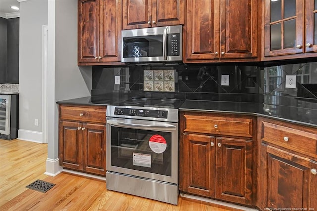 kitchen with beverage cooler, light wood-type flooring, appliances with stainless steel finishes, and tasteful backsplash