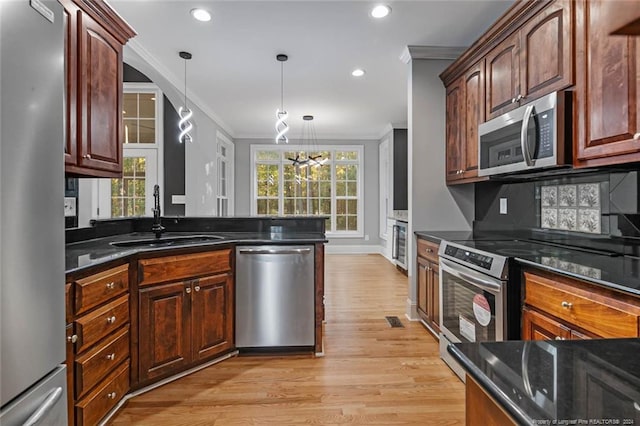 kitchen featuring sink, hanging light fixtures, light hardwood / wood-style floors, appliances with stainless steel finishes, and ornamental molding