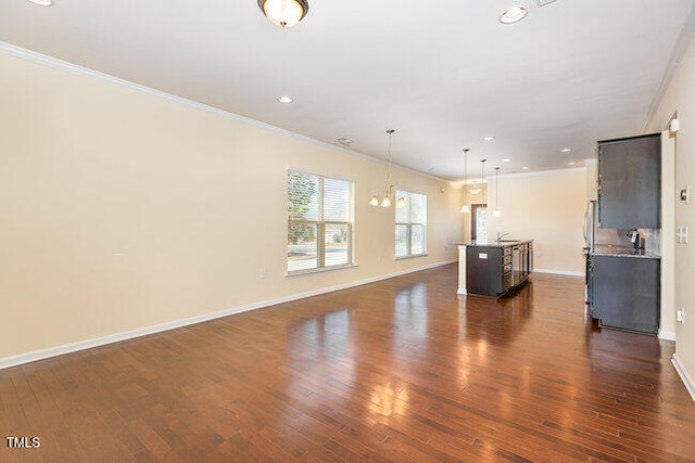 unfurnished living room with dark wood-type flooring, ornamental molding, baseboards, and an inviting chandelier