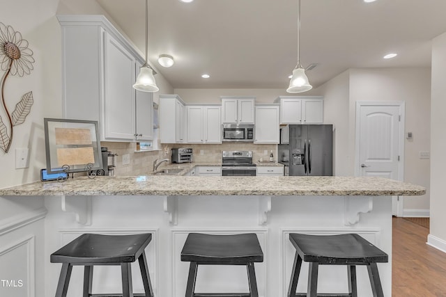 kitchen with a kitchen bar, appliances with stainless steel finishes, decorative backsplash, light hardwood / wood-style flooring, and white cabinetry