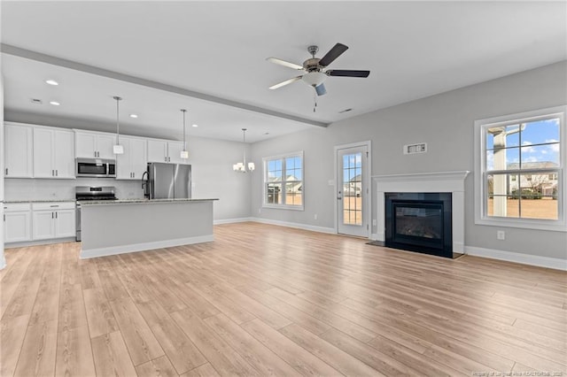 unfurnished living room with ceiling fan with notable chandelier and light hardwood / wood-style floors