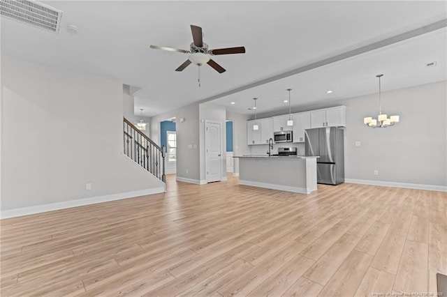 unfurnished living room with ceiling fan with notable chandelier and light hardwood / wood-style flooring