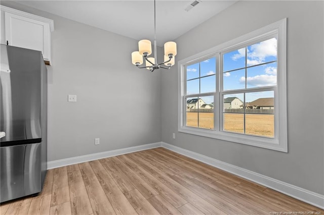 unfurnished dining area with light hardwood / wood-style floors, a chandelier, and a healthy amount of sunlight