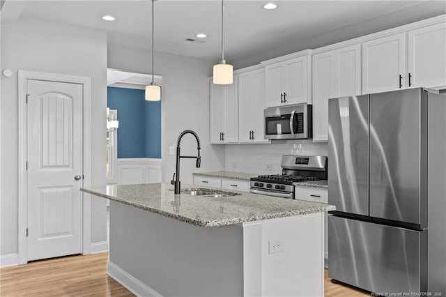 kitchen featuring sink, stainless steel appliances, white cabinets, and an island with sink