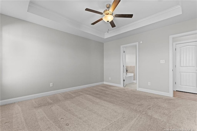 unfurnished bedroom featuring connected bathroom, light carpet, ceiling fan, a tray ceiling, and crown molding