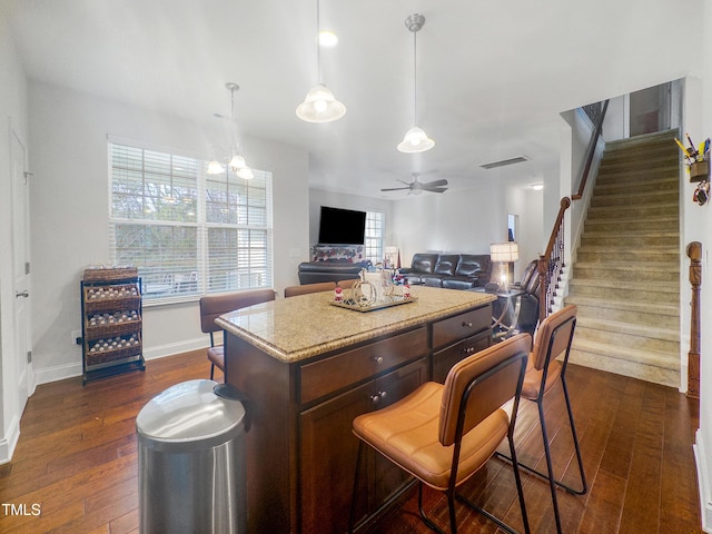 kitchen with dark hardwood / wood-style flooring, ceiling fan with notable chandelier, dark brown cabinetry, a center island, and hanging light fixtures