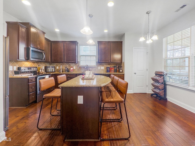 kitchen with a center island, stainless steel appliances, dark hardwood / wood-style flooring, decorative light fixtures, and a kitchen bar