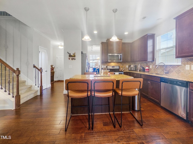 kitchen with sink, dark hardwood / wood-style flooring, pendant lighting, a kitchen island, and appliances with stainless steel finishes