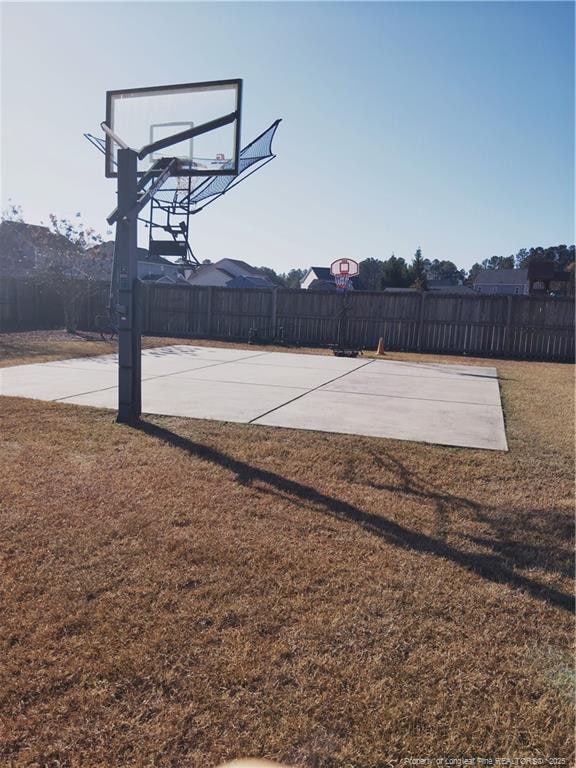 view of sport court with basketball hoop, fence, and a yard